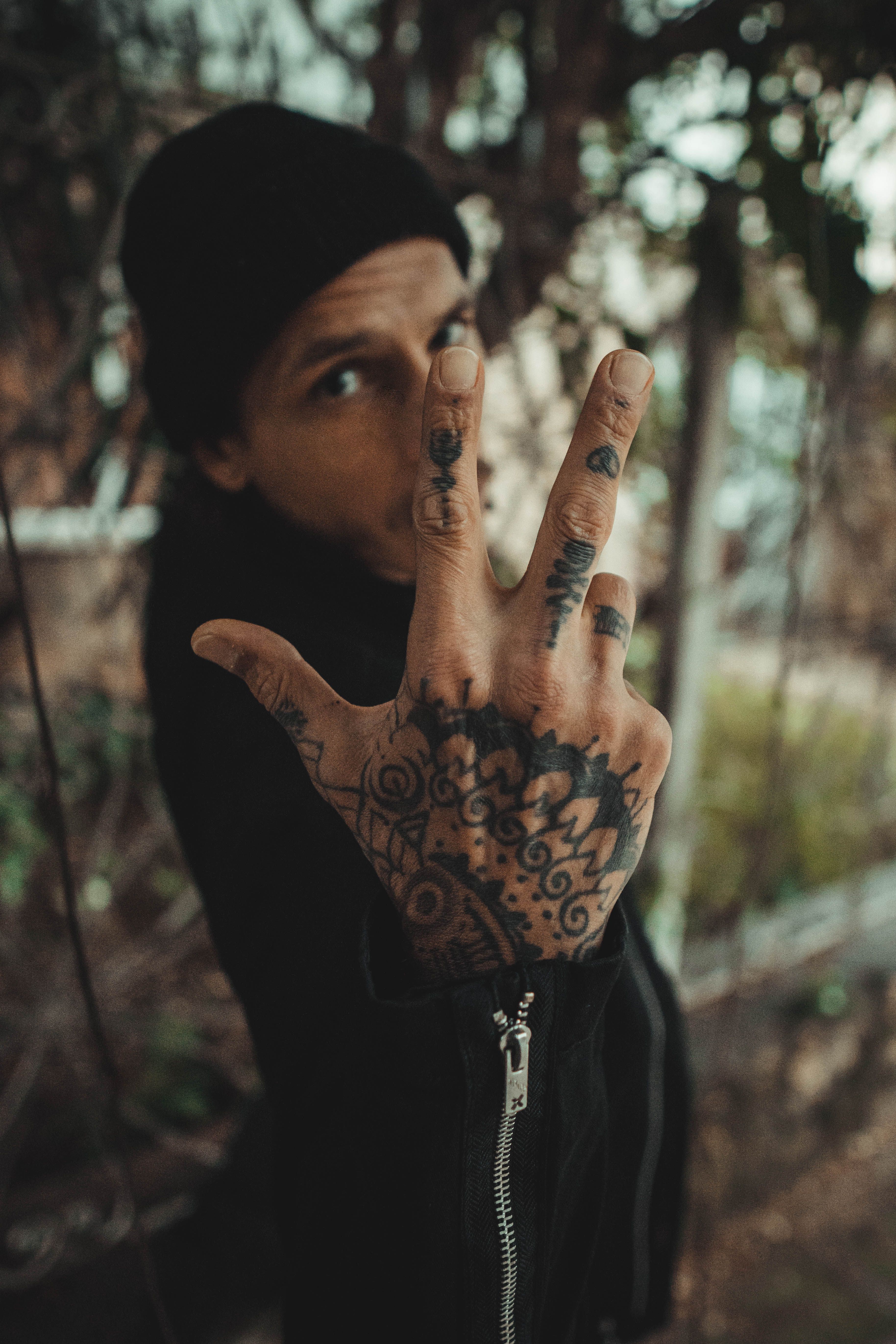 Mão fazendo sinal de paz com tatuagens nos dedos